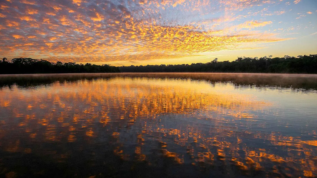 Sunset over Lake Sandoval with a canoe silhouetted on the water on a half-day Puerto Maldonado Amazon tour, Peru